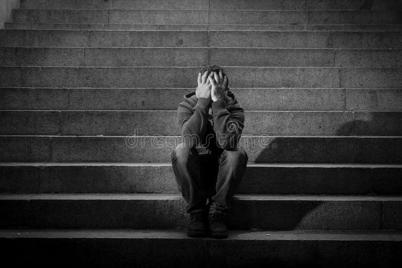 Молодой бездомный человек потерял в депрессии сидя на земных лестницах бетона улицы стоковое фото Молодой бездомный человек потерял в депрессии сидя на земных лестницах бетона улицы стоковое фото