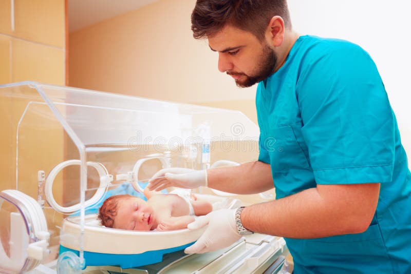 Молодой взрослый человек позаботить о newborn младенец в младенческом инкубаторе стоковая фотография Молодой взрослый человек позаботить о newborn младенец в младенческом инкубаторе стоковая фотография