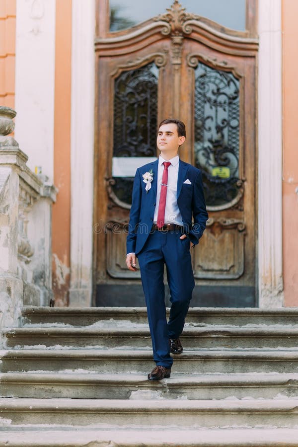 Молодой и уверенно groom новобрачных представляя в голубом костюме на старых лестницах на винтажном входе здания стоковые фотографии rf Молодой и уверенно groom новобрачных представляя в голубом костюме на старых лестницах на винтажном входе здания стоковые фотографии rf