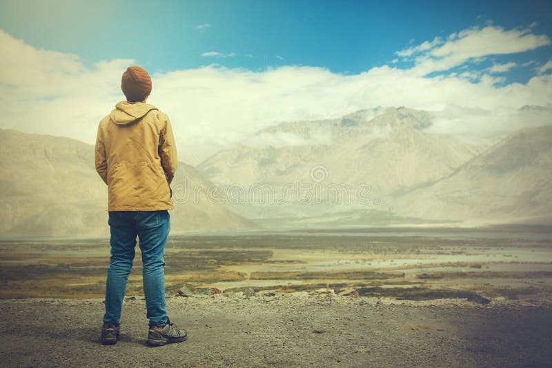 Молодой мужской путешественник стоя на скале песка, думая около или смотря вперед к что-то в Leh, Ladakh, Индия