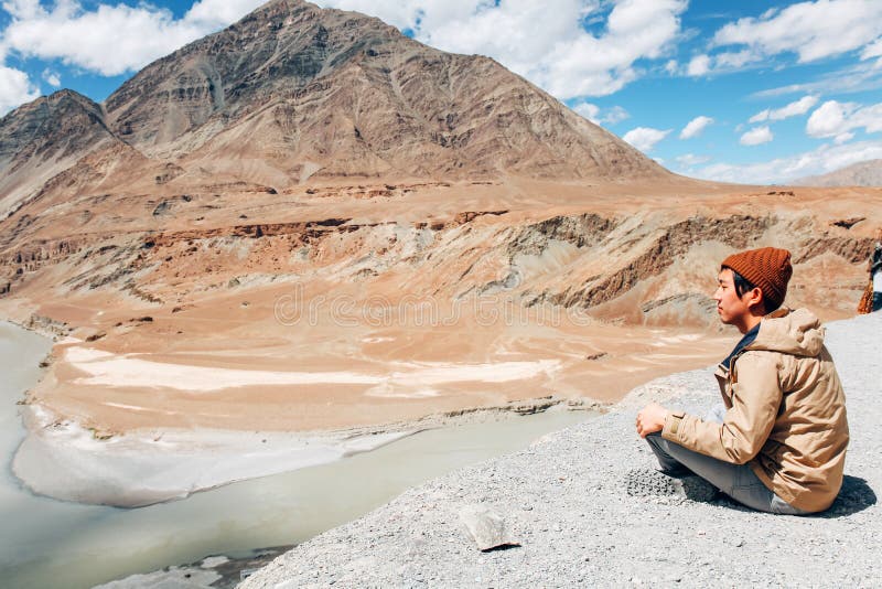 Молодой счастливый человек сидя на скале на отключении в река Инд в Leh, Ladakh, Индии стоковое изображение rf Молодой счастливый человек сидя на скале на отключении в река Инд в Leh, Ladakh, Индии стоковое изображение rf