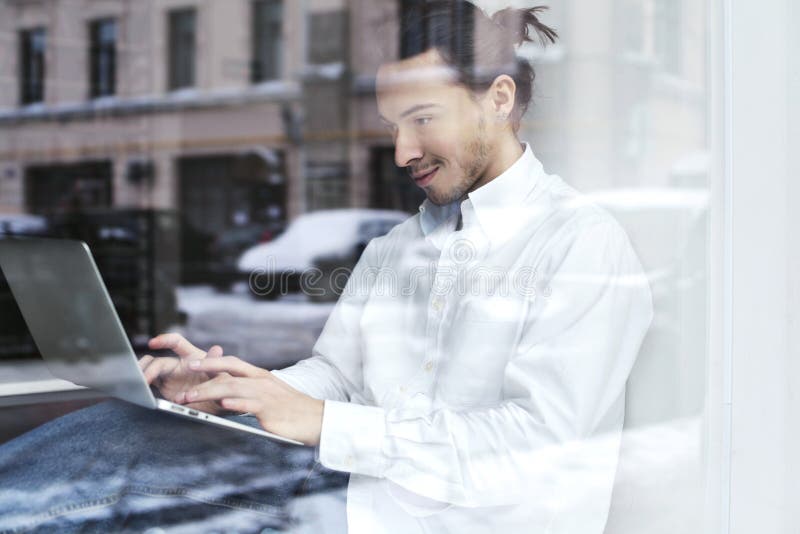 Молодые бизнесмен или студент сидя и работая на windowsill с открытой компьтер-книжкой на коленях стоковые фотографии rf Молодые бизнесмен или студент сидя и работая на windowsill с открытой компьтер-книжкой на коленях стоковые фотографии rf