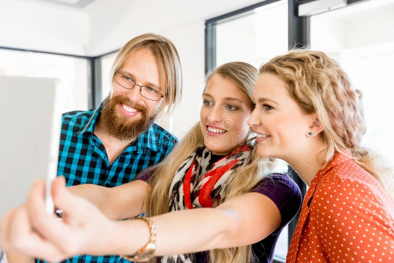 Молодые друзья принимая Selfie в офисе стоковое фото Молодые друзья принимая Selfie в офисе стоковое фото