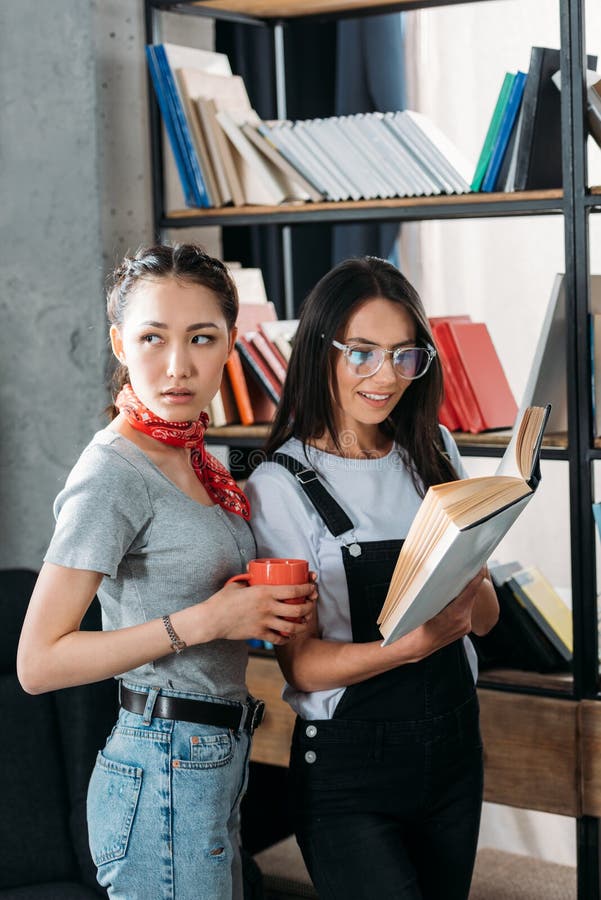Молодые студенты с книгой и чашкой изучая совместно и усмехаясь стоковое изображение rf Молодые студенты с книгой и чашкой изучая совместно и усмехаясь стоковое изображение rf