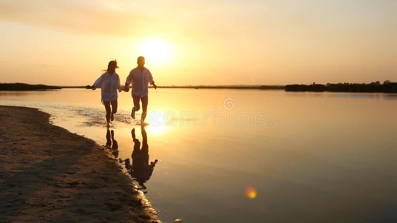 Молодые счастливые пары бежать к морю на заходе солнца