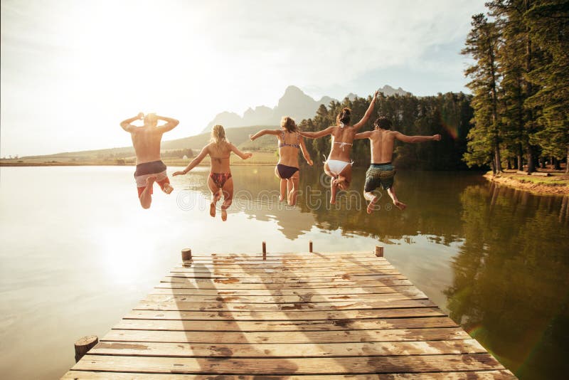 Молодые люди скача от пристани в озеро совместно