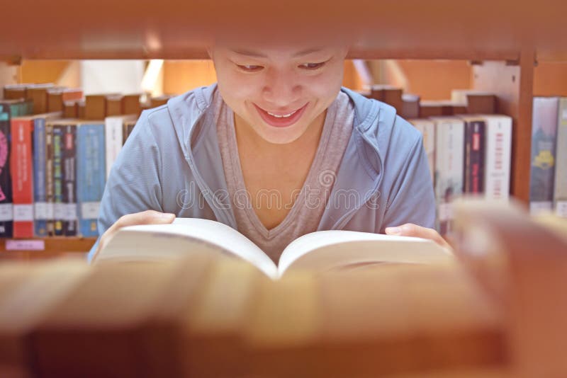 Молодая азиатская книга чтения студента университета женщины книжных полок в библиотеке колледжа для образования стоковые изображения rf