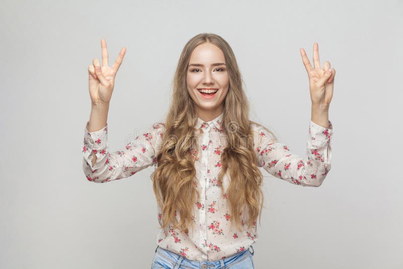 Young adult woman showing peace sign and toothy smiling. Studio shot. Young adult woman showing peace sign and toothy smiling. Studio shot