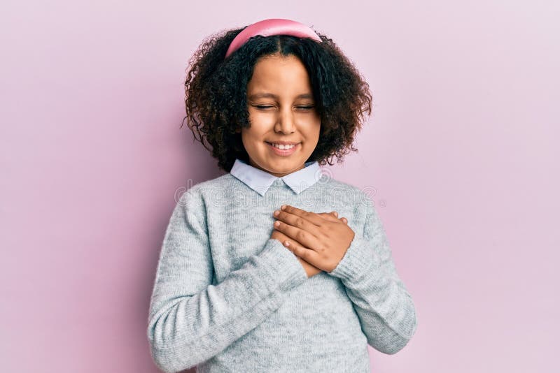 Young little girl with afro hair wearing casual clothes smiling with hands on chest with closed eyes and grateful gesture on face. health concept. Young little girl with afro hair wearing casual clothes smiling with hands on chest with closed eyes and grateful gesture on face. health concept
