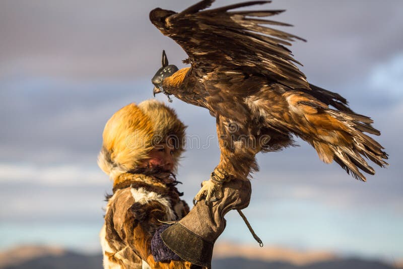 Молодая женщина Berkutchi Huntress орла казаха с лошадью пока охотящся к зайцам с беркуты на его оружиях стоковая фотография Молодая женщина Berkutchi Huntress орла казаха с лошадью пока охотящся к зайцам с беркуты на его оружиях стоковая фотография