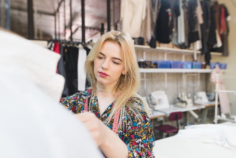 Молодая женщина dressmaker стоит в студии около маникюра с одеждами и работами Создавать стильные одежды стоковые фото Молодая женщина dressmaker стоит в студии около маникюра с одеждами и работами Создавать стильные одежды стоковые фото