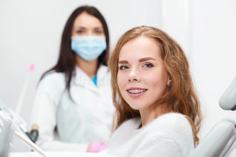 Happy red haired young women smiling to the camera wearing braces her dentist posing on the background copyspace medical treatment appointment medicine healthcare dentistry teeth. Happy red haired young women smiling to the camera wearing braces her dentist posing on the background copyspace medical treatment appointment medicine healthcare dentistry teeth.