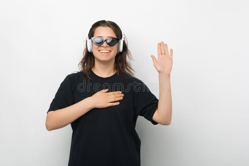 Young woman is making the promise or swear gesture while wearing headphones and sunglasses over white background. Young woman is making the promise or swear gesture while wearing headphones and sunglasses over white background.