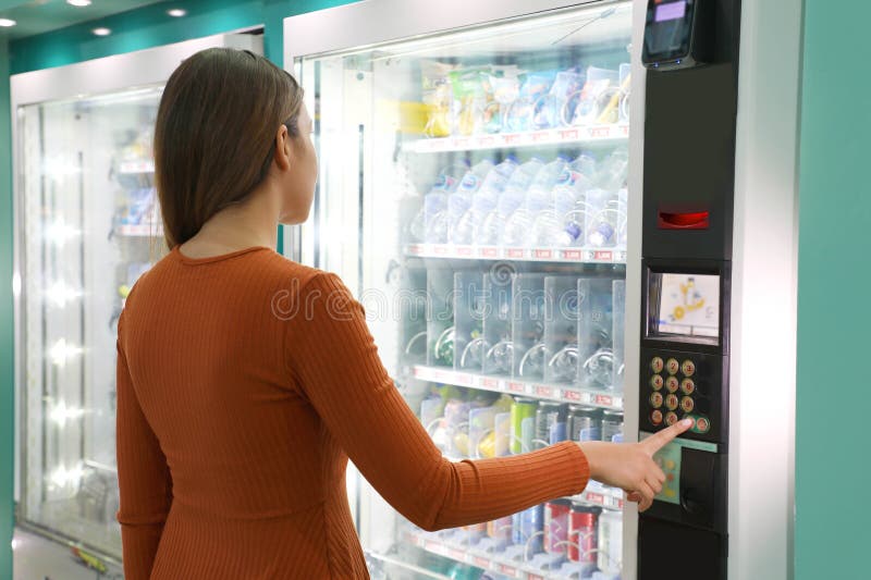 Молодая женщина путешественников при выборе закуски и напитки на автомате в аэропорту Автомат с девушкой