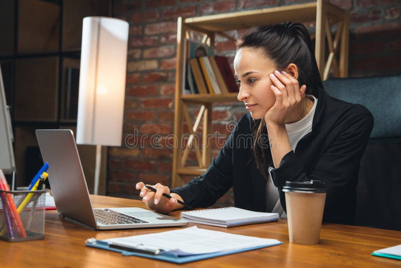 Interested, busy. Young woman working in modern office using devices and gadgets. Making reports, analitycs, routine processing tasks. Concept of business, finance, professional occupation. Interested, busy. Young woman working in modern office using devices and gadgets. Making reports, analitycs, routine processing tasks. Concept of business, finance, professional occupation.