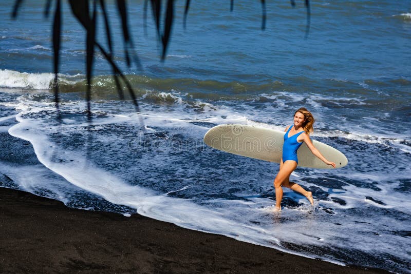 Молодая женщина с прогулкой surfboard на пляже отработанной формовочной смеси стоковое изображение rf Молодая женщина с прогулкой surfboard на пляже отработанной формовочной смеси стоковое изображение rf