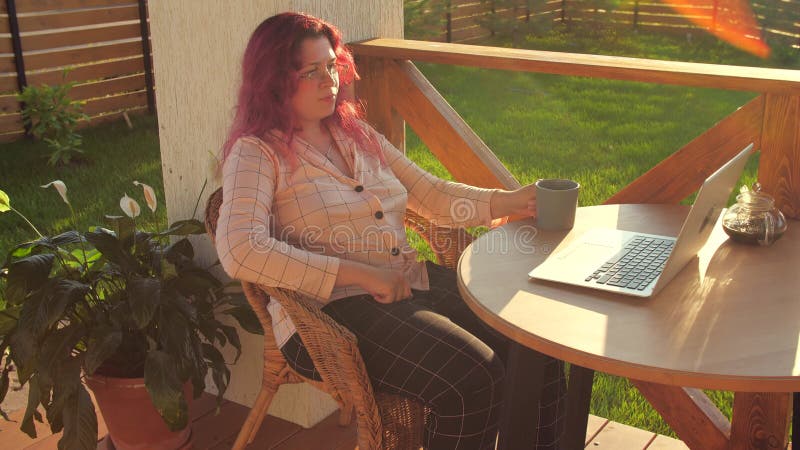 молодая женщина, смотрящая сериал в классе интернет-класса дистанционного образования на ноутбуке, пьёт тёплый чай на террасе свое