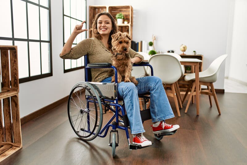 Young hispanic girl sitting on wheelchair at home smiling with hands on chest with closed eyes and grateful gesture on face. health concept. Young hispanic girl sitting on wheelchair at home smiling with hands on chest with closed eyes and grateful gesture on face. health concept