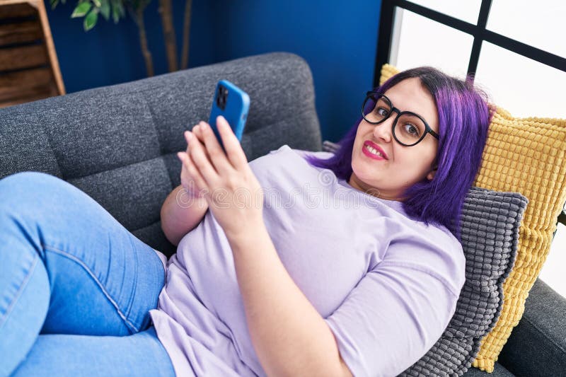 молодая красивая женщина plus size с помощью смартфона лежать на диване дома стоковые фотографии rf