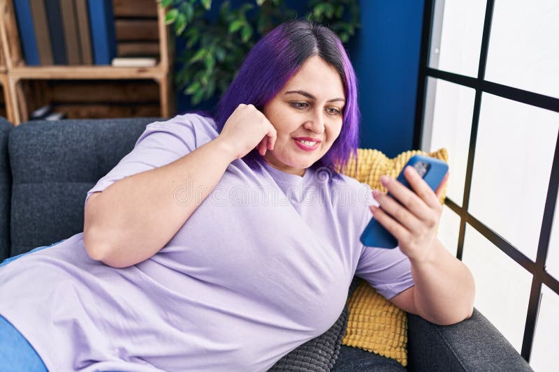молодая красивая женщина plus size с помощью смартфона лежать на диване дома стоковое фото