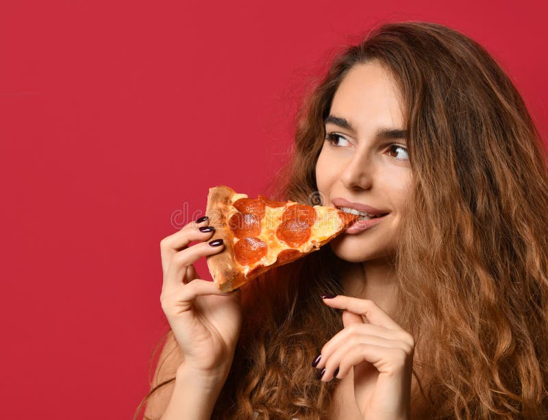 Молодая красивая женщина ест кусок пиццы pepperoni с закрытыми глазами усмехаясь на красном пинке стоковое фото rf Молодая красивая женщина ест кусок пиццы pepperoni с закрытыми глазами усмехаясь на красном пинке стоковое фото rf