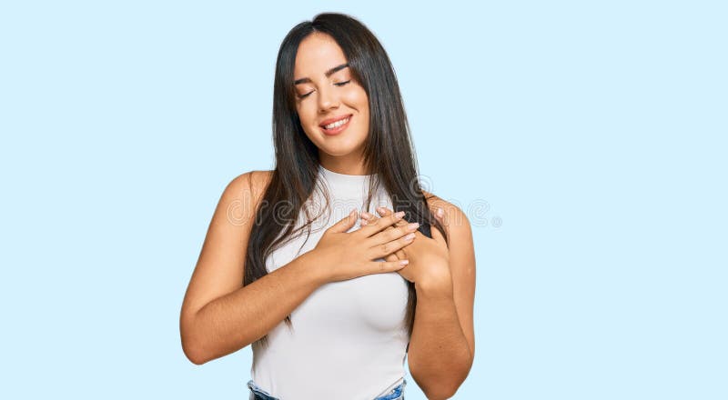 Young beautiful hispanic girl wearing casual clothes smiling with hands on chest with closed eyes and grateful gesture on face. health concept. Young beautiful hispanic girl wearing casual clothes smiling with hands on chest with closed eyes and grateful gesture on face. health concept