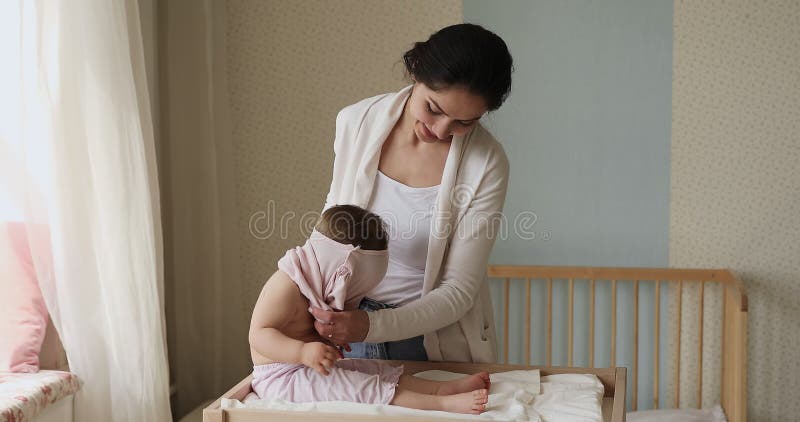 Молодая любящая мать одевает красивую младшую девочку
