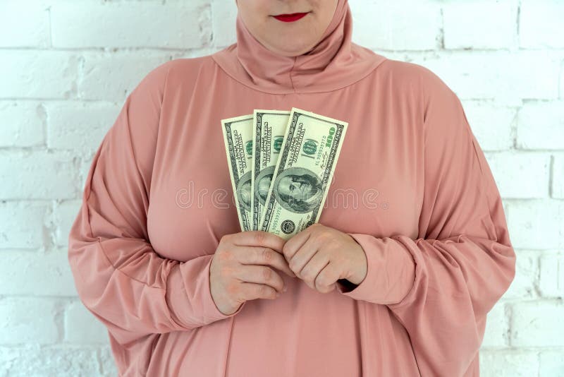 Молодая мусульманская женщина в розовых одеждах hijab держит денег наличных денег в банкнотах доллара и розария в ее руках стоковые фотографии rf Молодая мусульманская женщина в розовых одеждах hijab держит денег наличных денег в банкнотах доллара и розария в ее руках стоковые фотографии rf