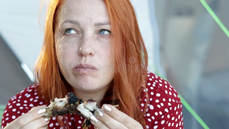 молодая рыжая женщина ест мясной стейк в кемпинге у палатки в сосновом лесу. сток-видео