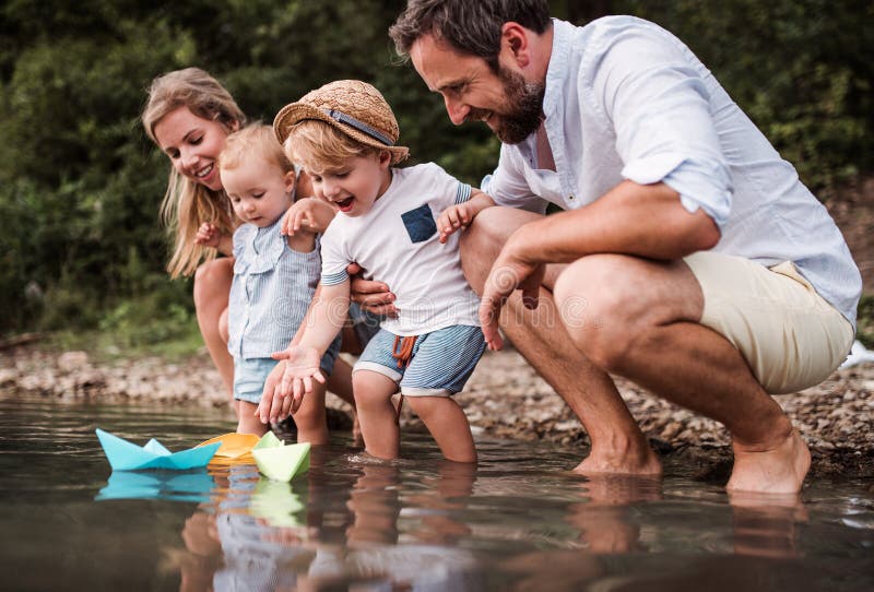 Молодая семья с 2 детьми малыша outdoors рекой летом, играя