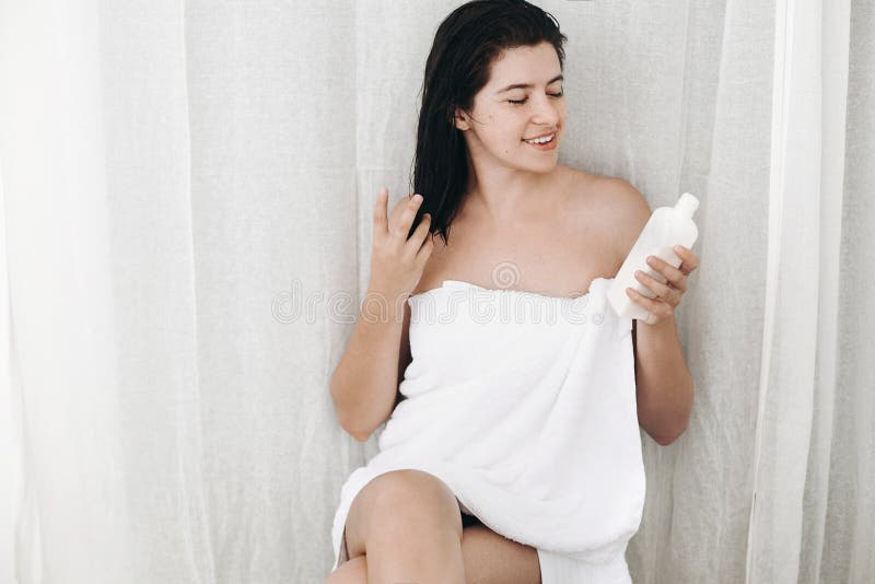 Молодая счастливая женщина в белом полотенце держа moisturizing сливк в бутылке в bathroom Забота кожи и тела Тонкий сексуальный стоковое фото Молодая счастливая женщина в белом полотенце держа moisturizing сливк в бутылке в bathroom Забота кожи и тела Тонкий сексуальный стоковое фото