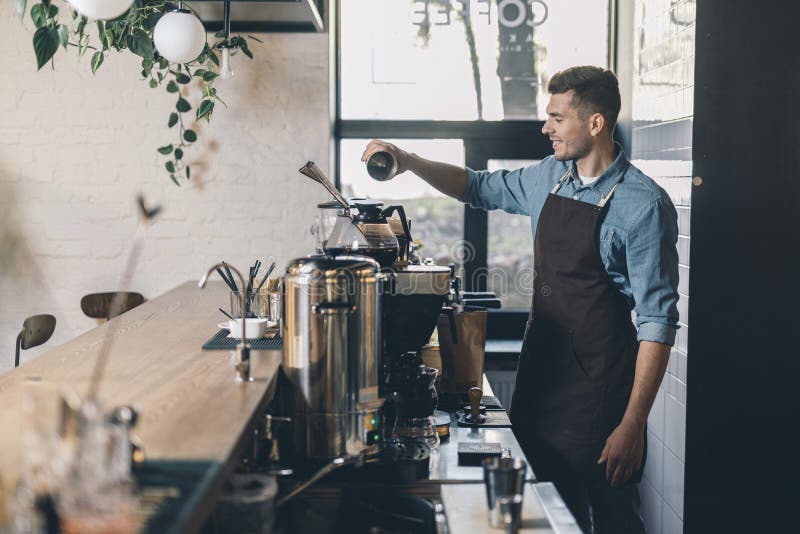 Молодое barista просеивая кофе в танк и усмехаться зерна стоковая фотография Молодое barista просеивая кофе в танк и усмехаться зерна стоковая фотография