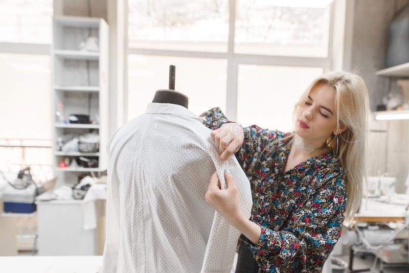 Молодой женский dressmaker работает иглы вставок в одежды которые на манекене стоковые фотографии rf Молодой женский dressmaker работает иглы вставок в одежды которые на манекене стоковые фотографии rf