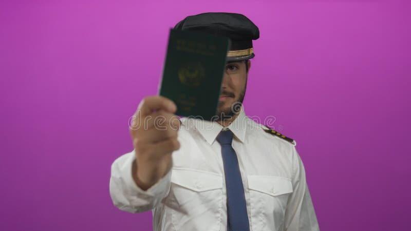 Молодой латиноамериканский пилот с зеленым паспортом на фоне ярко-розового цвета одет в форму с уверенным сток-видео