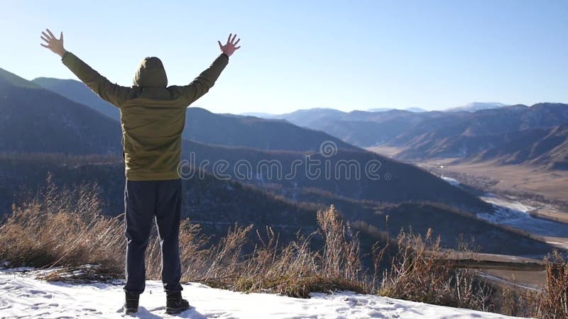 Молодой человек в куртке, стоя na górze горы, смотрит вне в расстояние и чувствует свободу и утеху от a