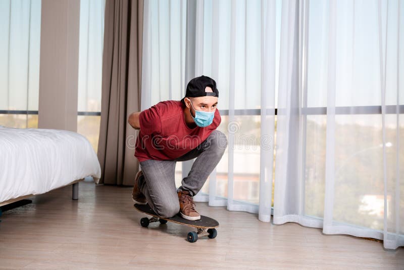 Молодой человек в медицинской маске на longboard. Домашний интерьер. На фоне окна. Концепция карантина и деятельности стоковая фотография