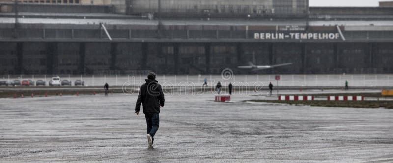 Молодой человек идя к зданию Берлину Германии авиаполя tempelhof стоковые изображения Молодой человек идя к зданию Берлину Германии авиаполя tempelhof стоковые изображения
