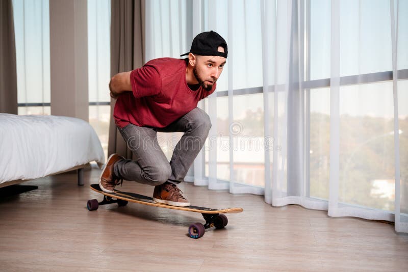 Молодой человек на longboard представляет, что он управляет вниз по улице. Крытый. Концепция карантина и дома. Копия стоковая фотография