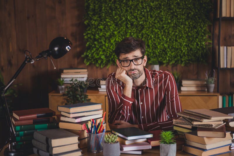 Молодой человек учится дома в окружении книг и зелени, демонстрируя вдумчивое выражение стоковые изображения