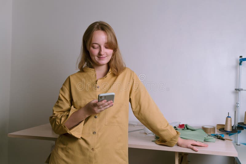 Молодые женщины standingn белошвейки в магазине портного и смотреть на нее смартфон связать клиент стоковая фотография