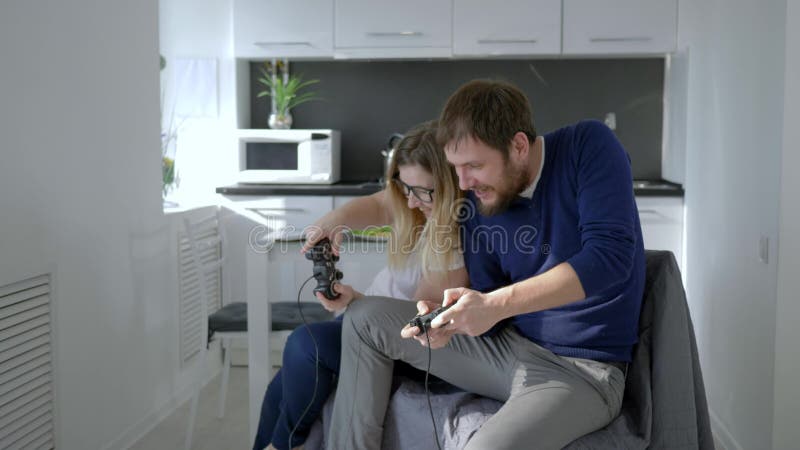 Молодые пары играя видеоигру и нажимая один другого пока сидящ на кресле