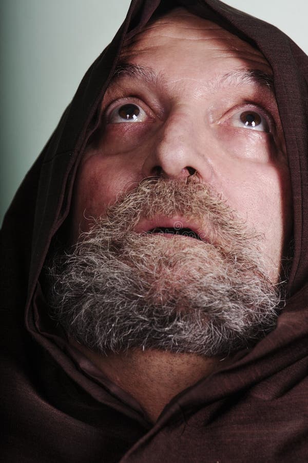 Capuchin monk with a beard illuminated by faith praying god. A monk with his robe looks up at the sky with eyes wide open. Concept of vocation to God. Capuchin monk with a beard illuminated by faith praying god. A monk with his robe looks up at the sky with eyes wide open. Concept of vocation to God.