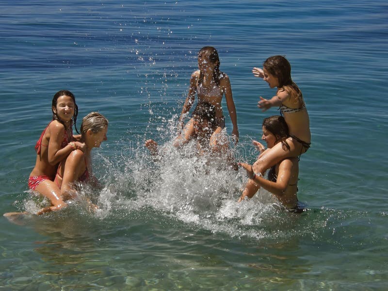 Four cute sisters (best friends) with mother and brother standing in the sea (piggy back) - spend summer holidays (have a fun and games - make foam sea spray with hands) in the clear Adriatic Sea in Croatia. Horizontal color photo. Four cute sisters (best friends) with mother and brother standing in the sea (piggy back) - spend summer holidays (have a fun and games - make foam sea spray with hands) in the clear Adriatic Sea in Croatia. Horizontal color photo.
