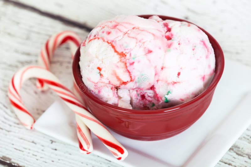 Peppermint ice cream in a red bowl and candy canes against white wooden background. Peppermint ice cream in a red bowl and candy canes against white wooden background