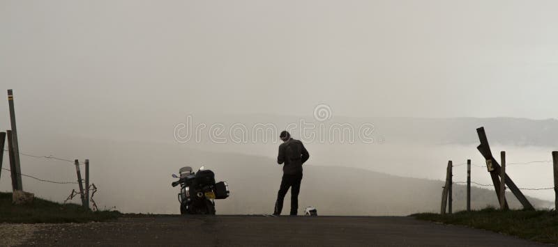 Мотоцикл и стоящий всадник silhouetted против туманной долины стоковые изображения Мотоцикл и стоящий всадник silhouetted против туманной долины стоковые изображения