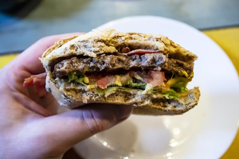 Мужская рука держа сдержанный, очень вкусный cheeseburger, на фоне плиты стоковая фотография rf Мужская рука держа сдержанный, очень вкусный cheeseburger, на фоне плиты стоковая фотография rf