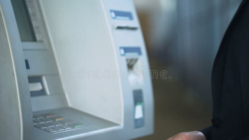 Мужские руки входя в код штыря на клавиатуре ATM, разделяя деньги от учета