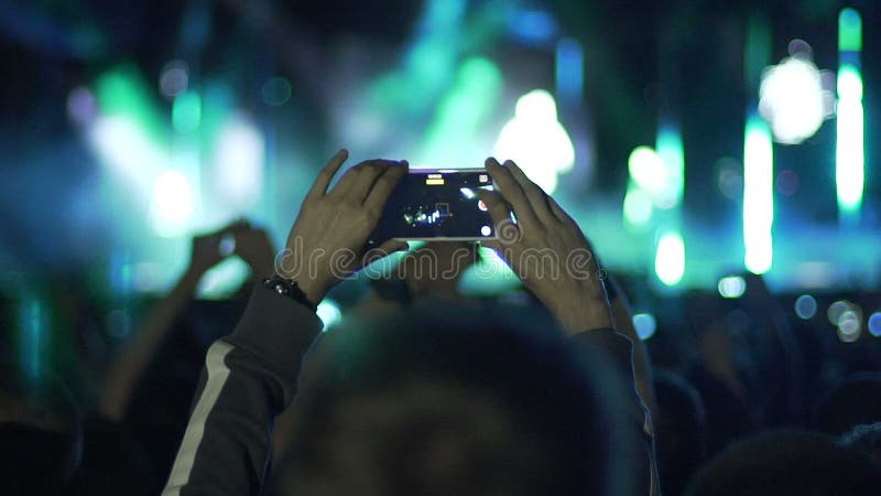 Мужские руки держа smartphone в воздухе, снимая изумительную выставку на этапе, медленн-mo