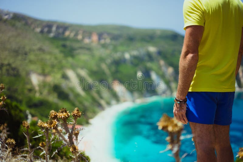 Мужские туристские нося шорты на пляже Kefalonia Petani наслаждаясь живописной панорамой изумрудной лазурной лагуны залива стоковые изображения rf Мужские туристские нося шорты на пляже Kefalonia Petani наслаждаясь живописной панорамой изумрудной лазурной лагуны залива стоковые изображения rf