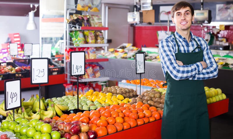 Мужской продавец представляя с яблоками, tangerines и бананами в магазине стоковое изображение rf Мужской продавец представляя с яблоками, tangerines и бананами в магазине стоковое изображение rf